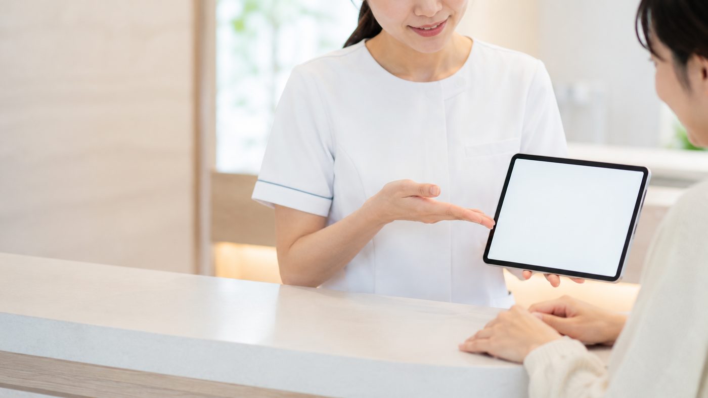 カウンターでタブレットを見せながら見積内容を説明する歯科スタッフ